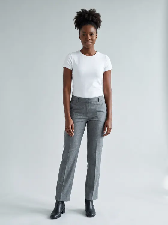 Woman with curly hair in a high puff wearing a white t-shirt, mid-grey trousers and black ankle boots, full length