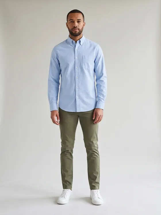 The same man in the same olive chinos, now wearing a pale light blue oxford button-down shirt