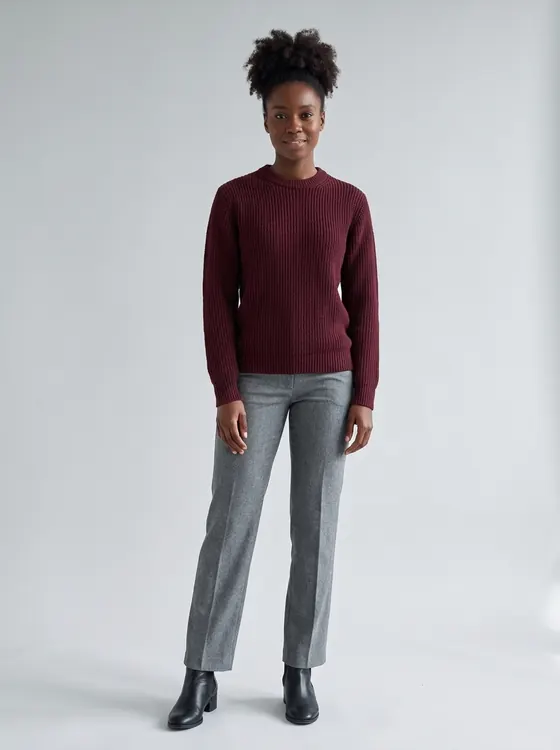 The same woman in the same grey trousers and black boots, now wearing a deep burgundy ribbed crewneck sweater